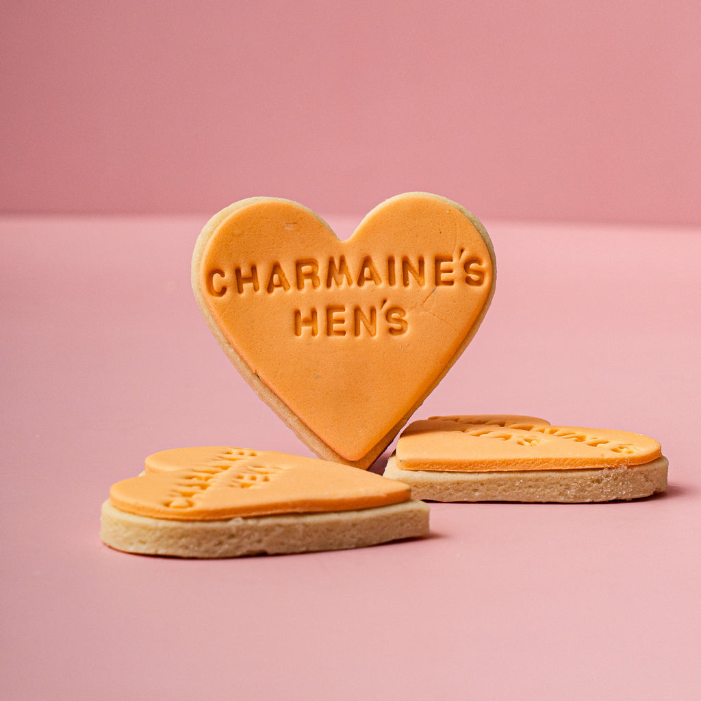 Heart-shaped cookies with 'CHARMAINE'S HEN'S' text on a pink background