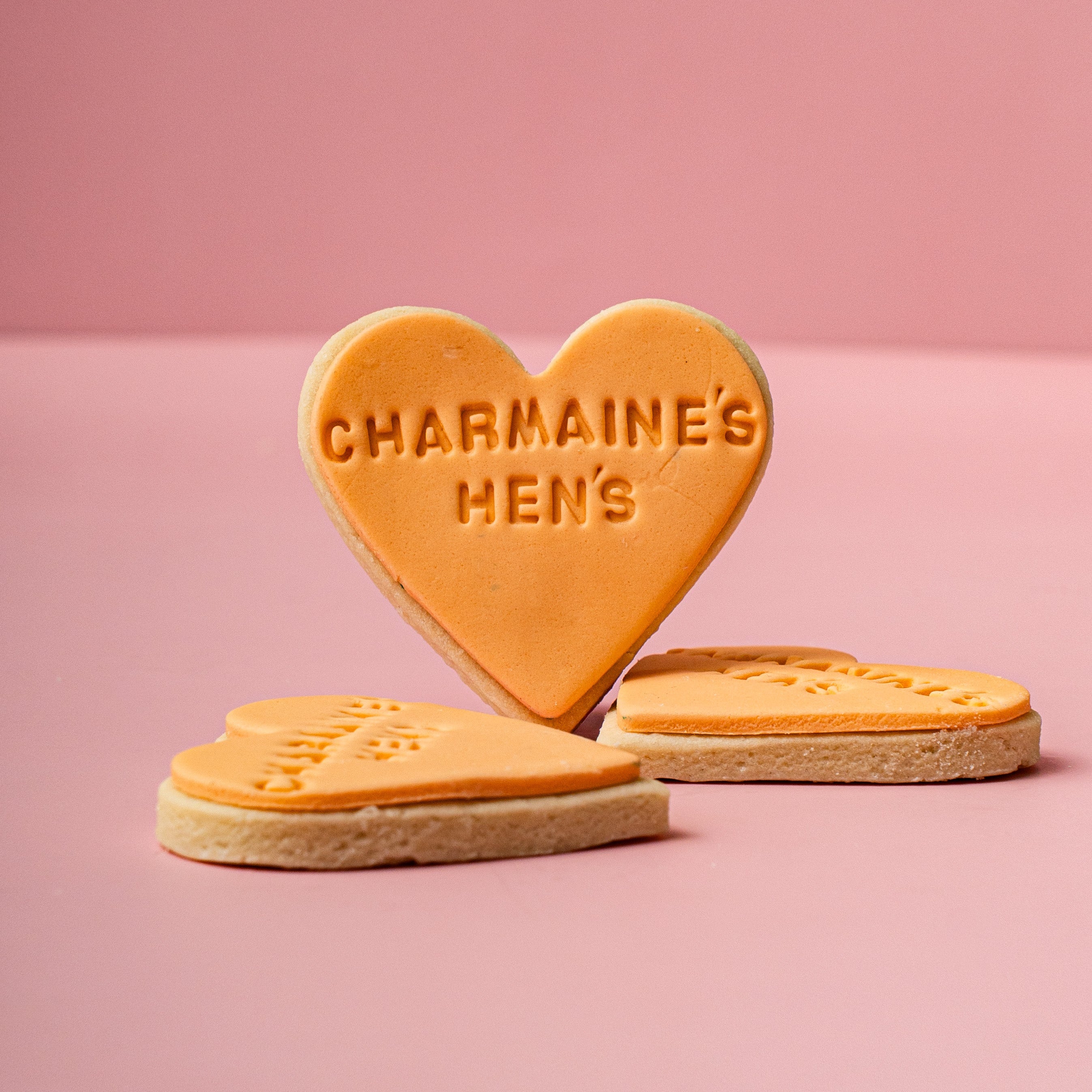 Heart-shaped cookies with 'CHARMAINE'S HEN'S' text on a pink background