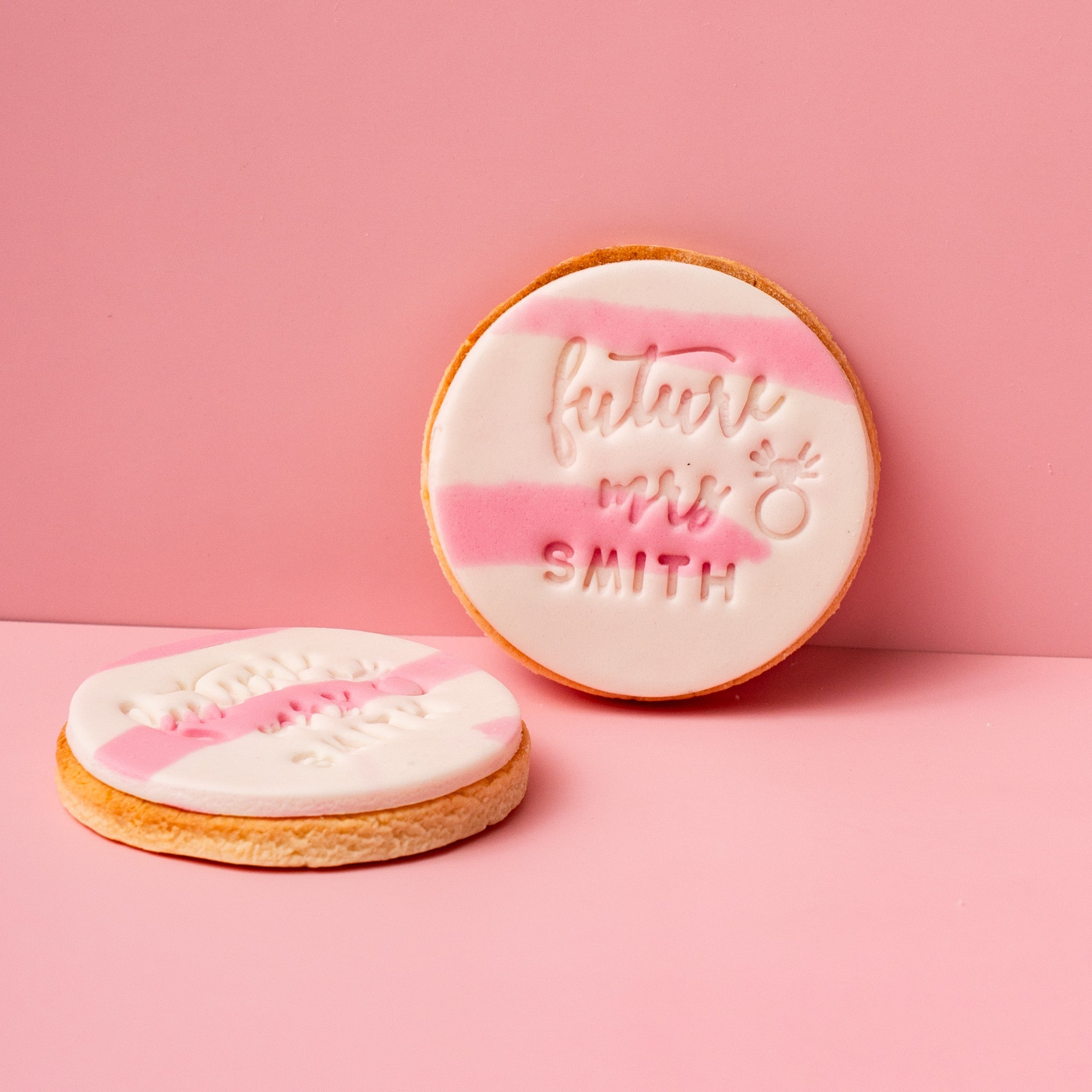 Two cookies with personalized text on a pink background