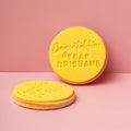 Two yellow cookies with 'Congratulations Team Brisbane' text on a pink background