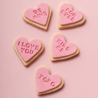 Heart-shaped cookies with Valentine's Day messages on a pink background