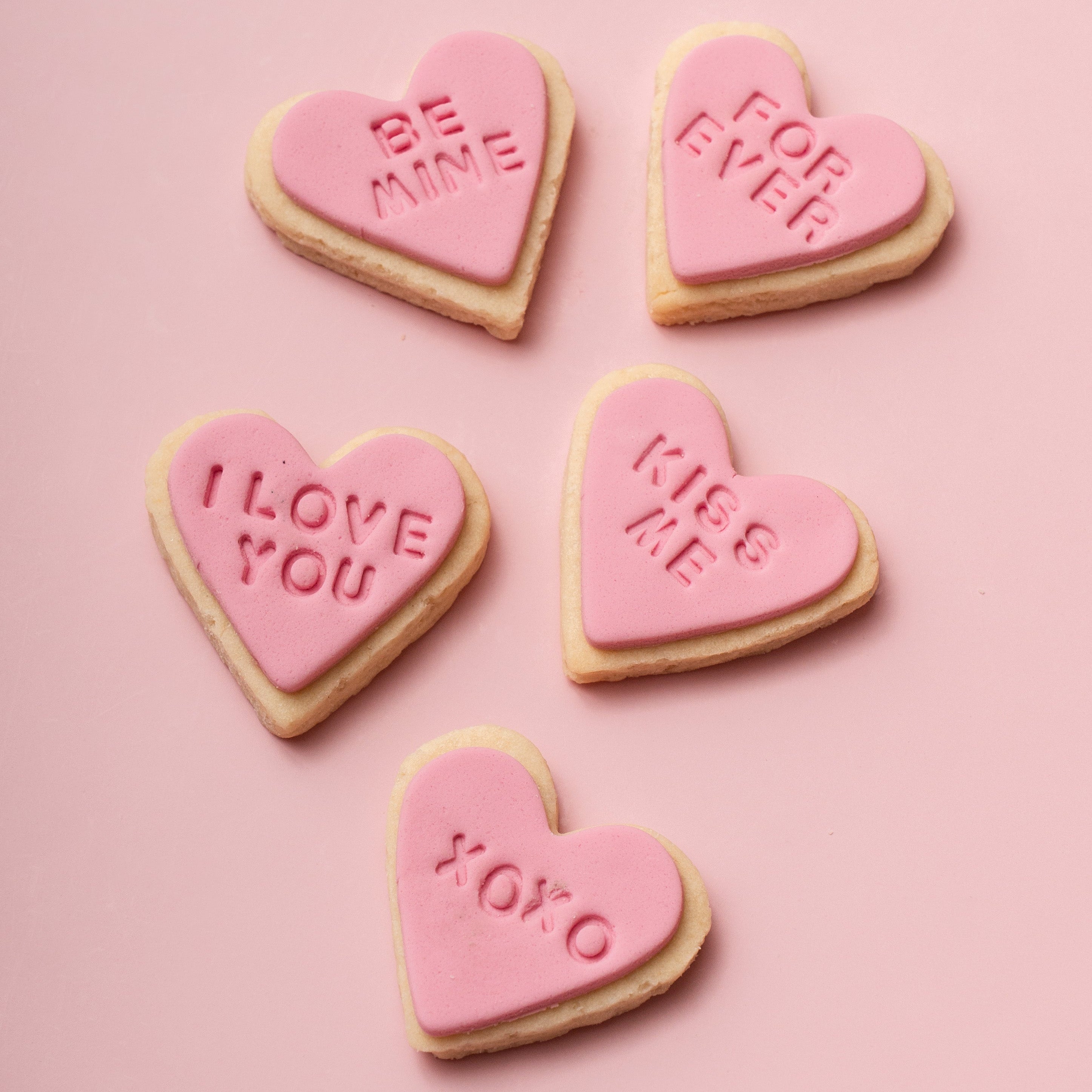 Heart-shaped cookies with Valentine's Day messages on a pink background