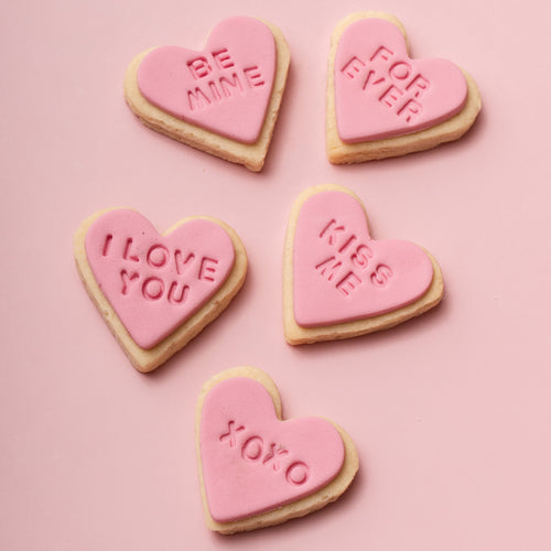 Heart-shaped cookies with Valentine's Day messages on a pink background