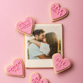 Heart-shaped cookies with suggestive text around a photo of a couple on a pink background