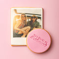 Cookie with 'Will you be my bridesmaid?' text next to a photo of two women on a pink background