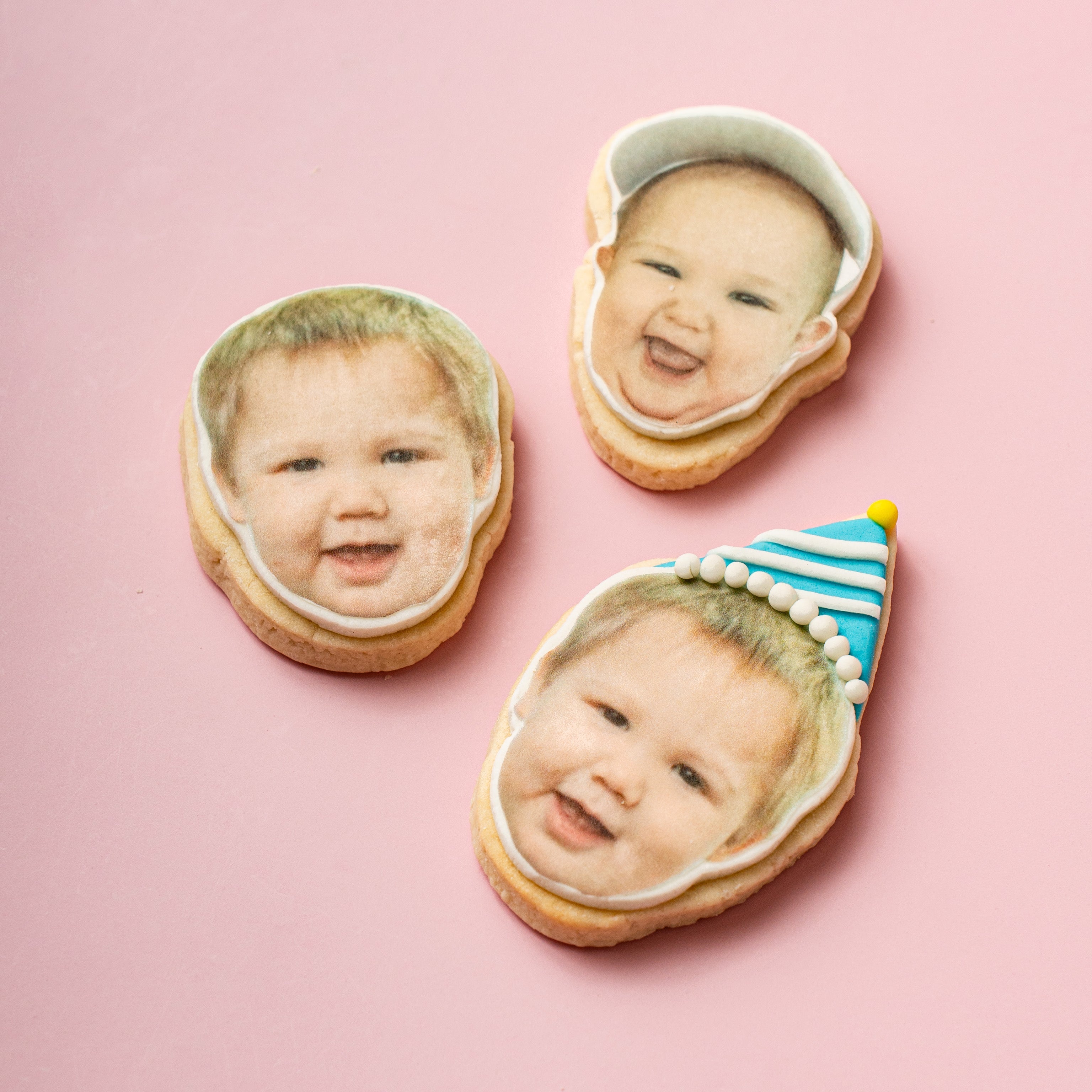 Three cookies with faces of a baby on a pink background