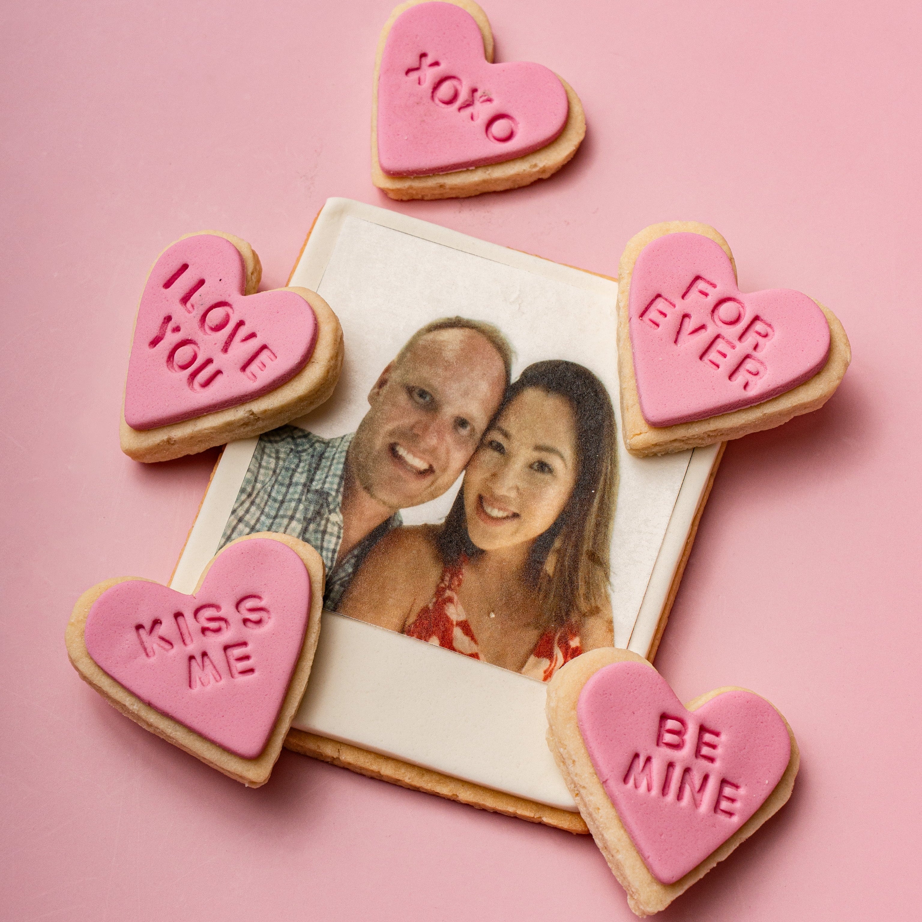 Heart-shaped cookies with Valentine's Day messages around a photo of a couple on a pink background